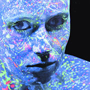 Girl with an ultra-violet blue-skin color to her face, looking at camera - paint splatter all over her face.