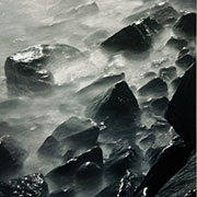 A long exposure of waves splashing over rocks at night.